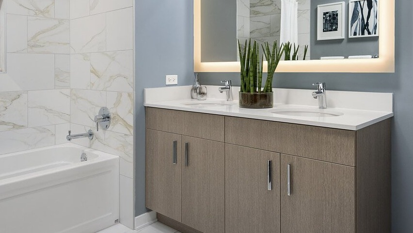 A contemporary bathroom featuring a deep soaking tub, a double vanity with an illuminated mirror, and stylish decor at The Sinclair in Chicago