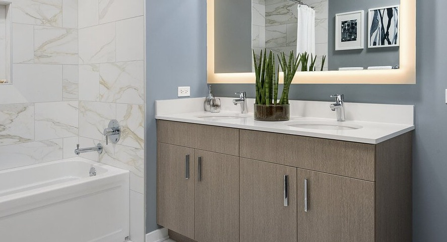 A contemporary bathroom featuring a deep soaking tub, a double vanity with an illuminated mirror, and stylish decor at The Sinclair in Chicago