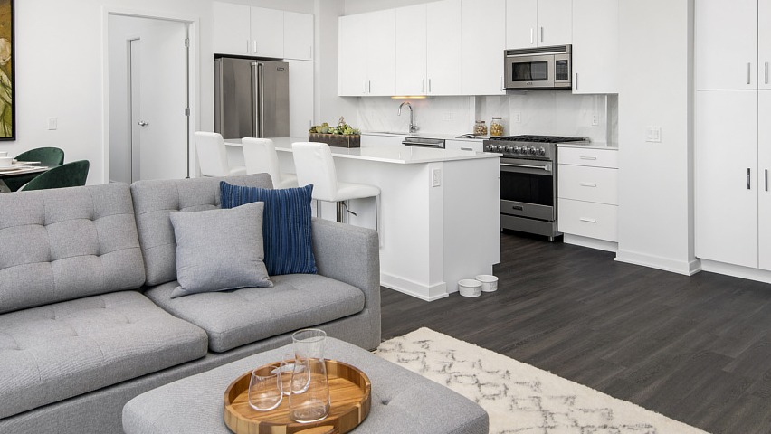 A bright open-concept apartment with a modern white kitchen, kitchen island seating, and a comfortable living area at The Sinclair in Chicago