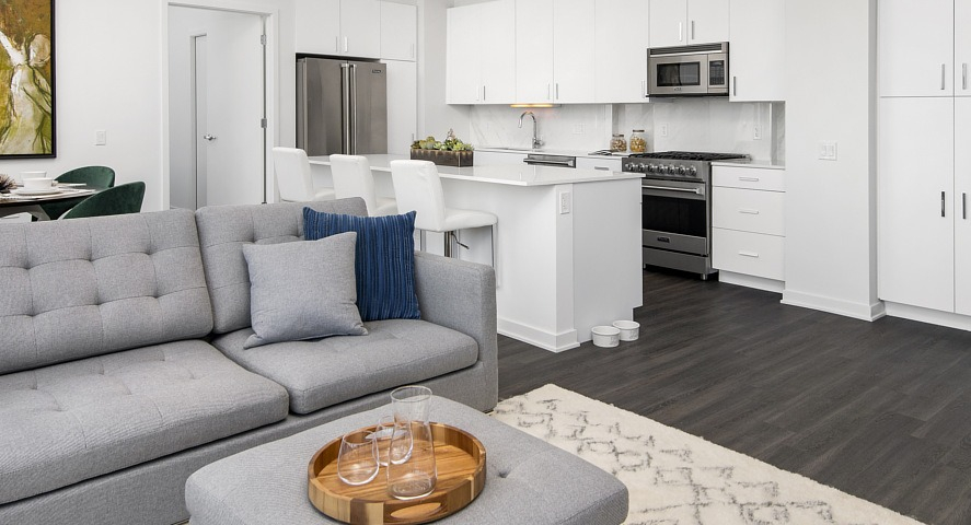 A bright open-concept apartment with a modern white kitchen, kitchen island seating, and a comfortable living area at The Sinclair in Chicago