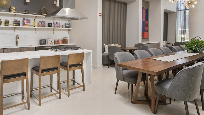 A modern resident kitchen with a large island and bar seating, alongside a spacious dining table and lounge area at The Sinclair in Chicago