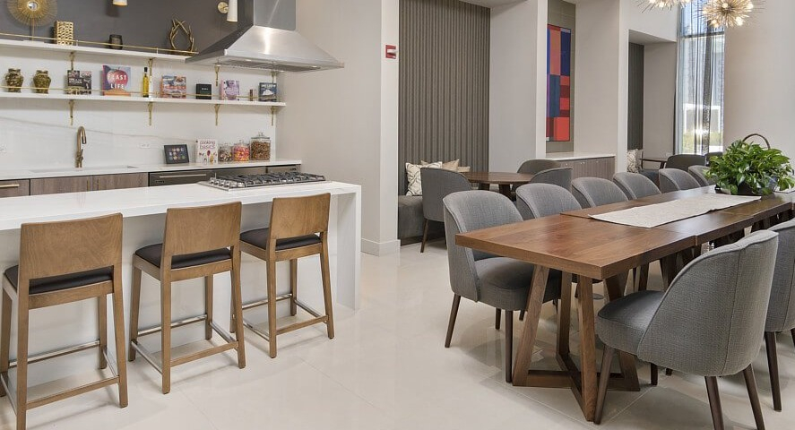 A modern resident kitchen with a large island and bar seating, alongside a spacious dining table and lounge area at The Sinclair in Chicago