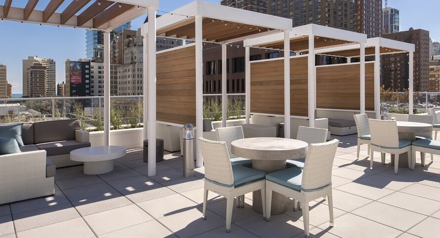 A stylish rooftop lounge area featuring comfortable outdoor sofas under pergolas and dining tables, perfect for socializing at The Sinclair in Chicago