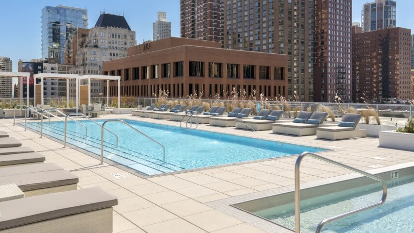 A luxurious rooftop pool deck with a swimming pool, separate hot tub, and multiple lounge chairs, offering urban skyline views at The Sinclair in Chicago