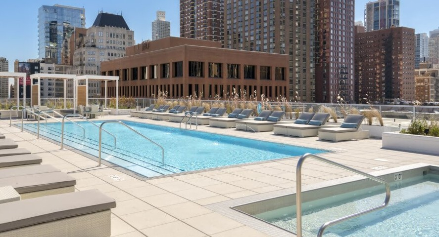 A luxurious rooftop pool deck with a swimming pool, separate hot tub, and multiple lounge chairs, offering urban skyline views at The Sinclair in Chicago