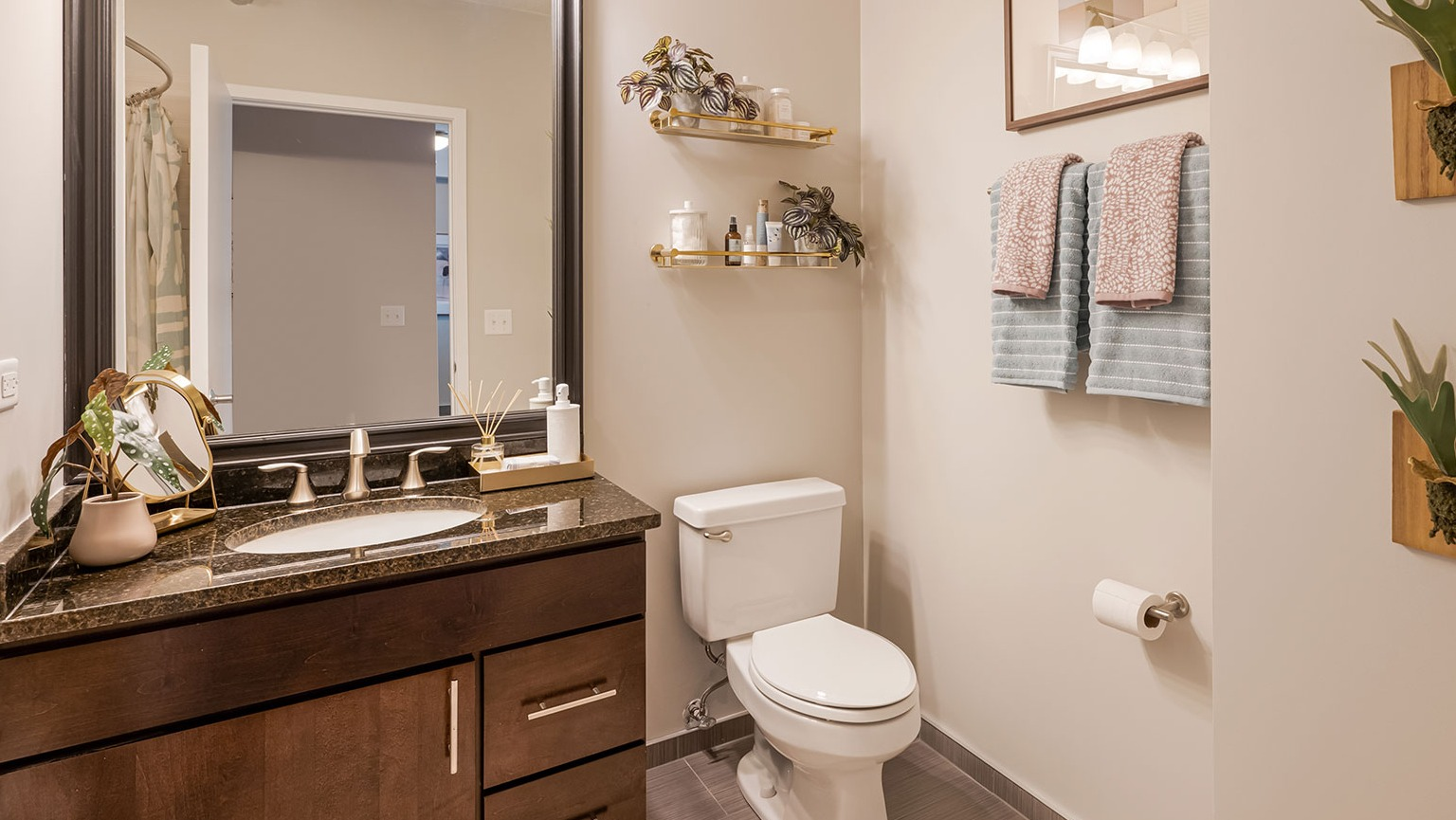 A sleek bathroom with a dark wood vanity, a large mirror, and a combined shower-tub area with decorative wall plants at The Streeter in Chicago