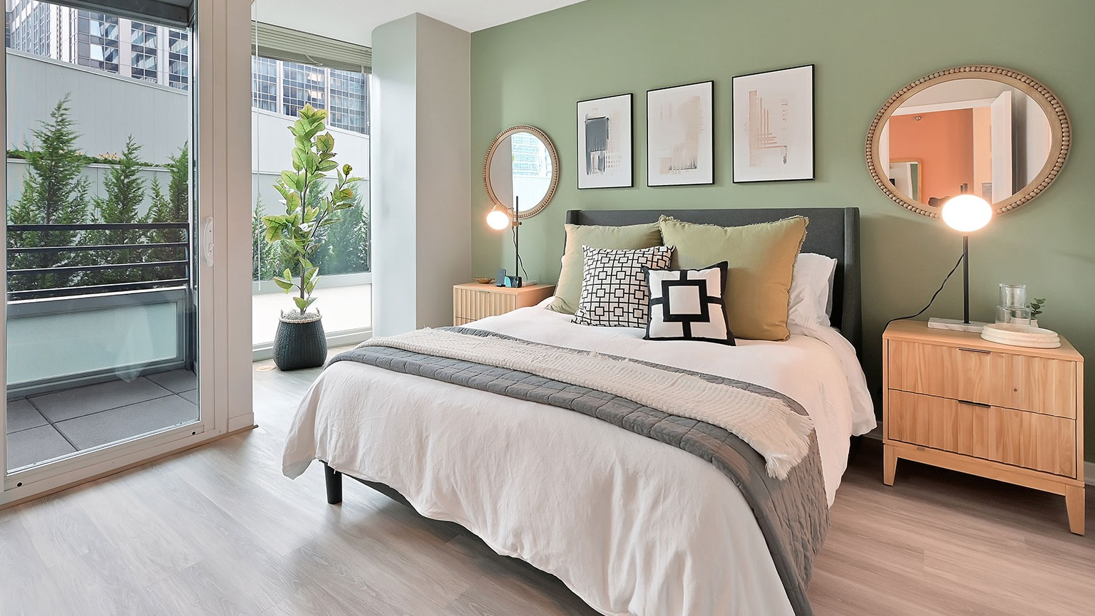 A modern bedroom with a comfortable bed, a stylish green accent wall, and a private balcony overlooking the city at The Streeter in Chicago