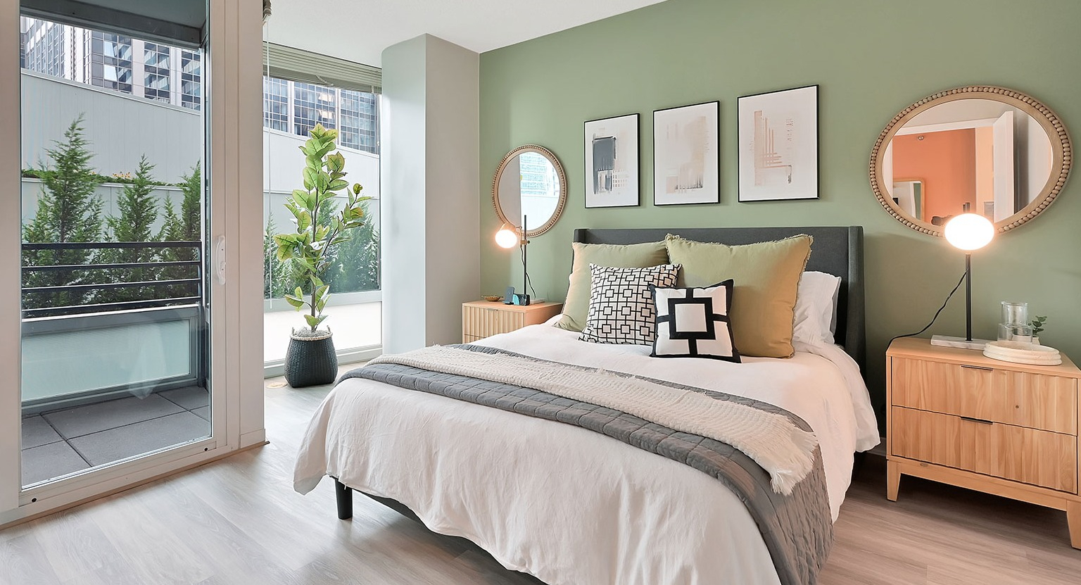 A modern bedroom with a comfortable bed, a stylish green accent wall, and a private balcony overlooking the city at The Streeter in Chicago