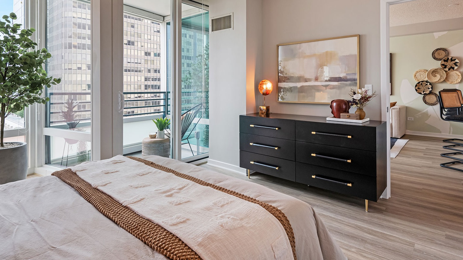 A modern bedroom with elegant decor, a large dresser, and a private balcony access with city views at The Streeter in Chicago