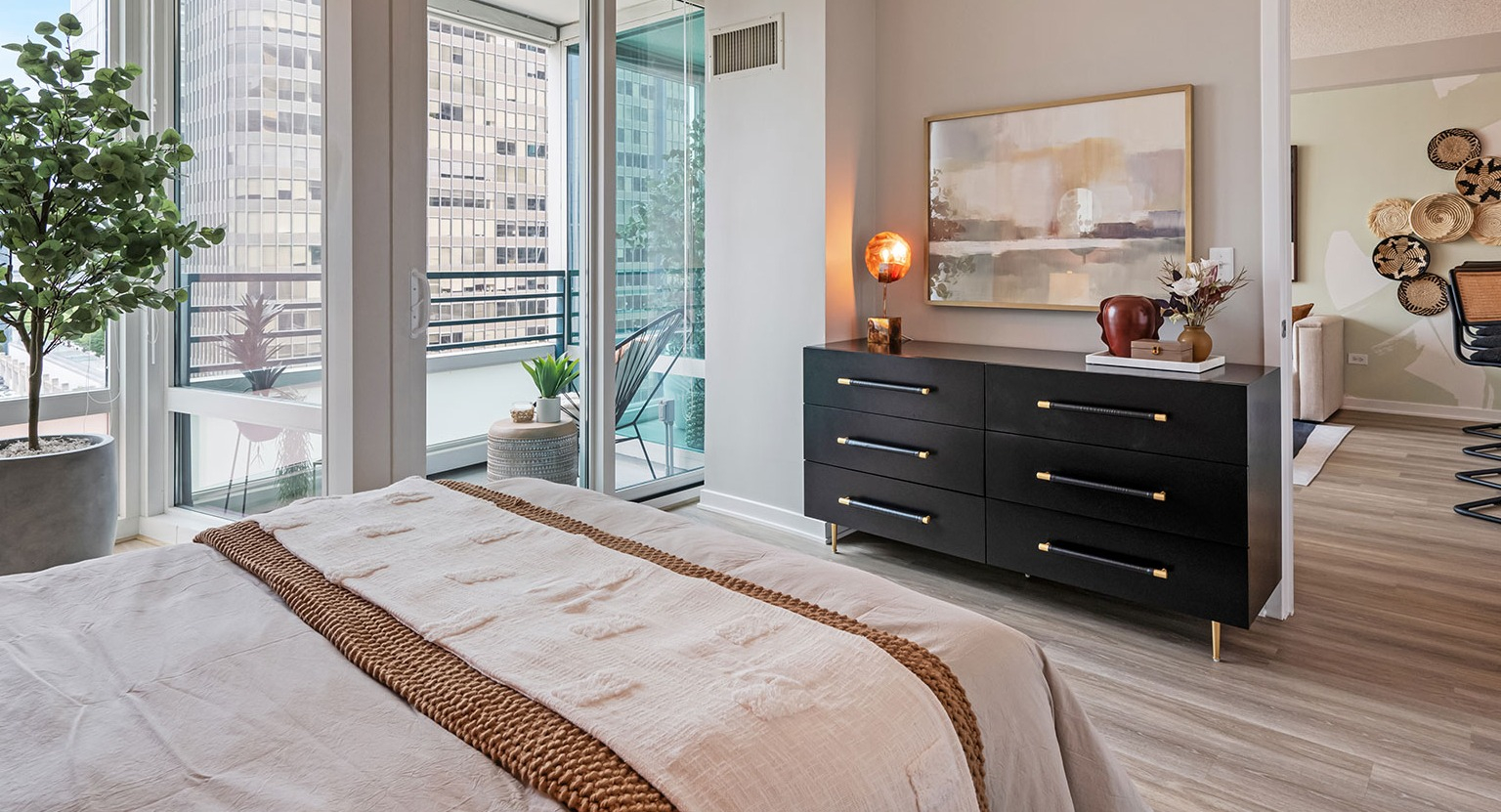 A modern bedroom with elegant decor, a large dresser, and a private balcony access with city views at The Streeter in Chicago