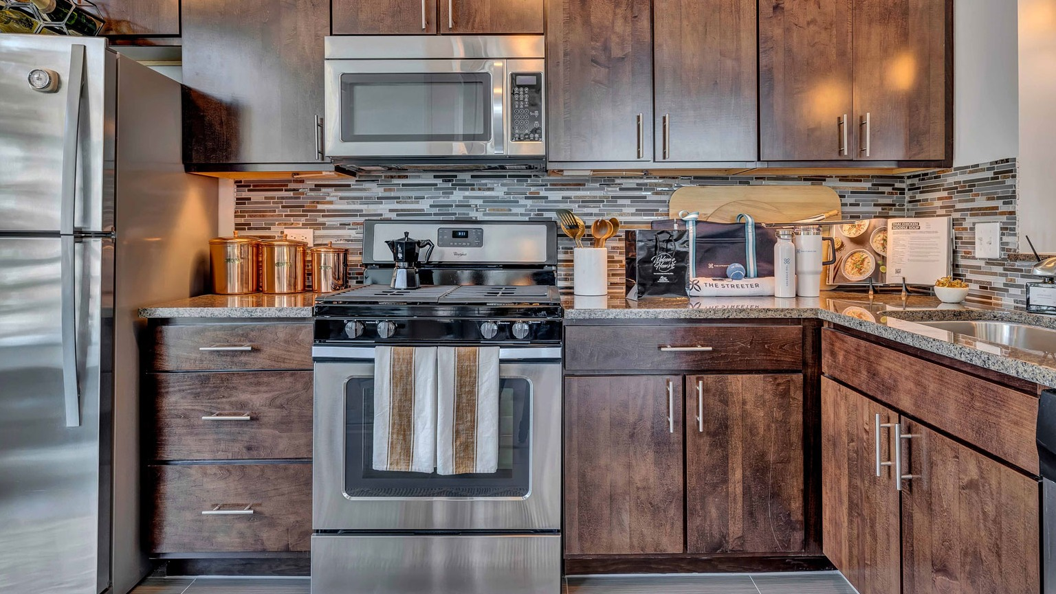 A stylish gourmet kitchen with rich dark wood cabinets, granite countertops, stainless steel appliances, and a mosaic backsplash at The Streeter in Chicago