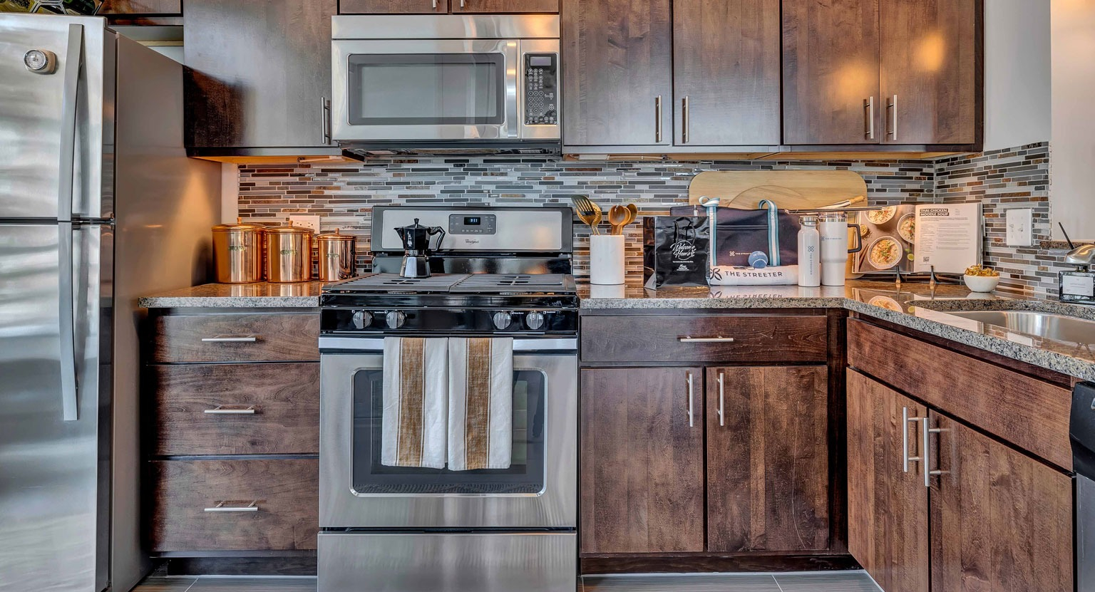 A stylish gourmet kitchen with rich dark wood cabinets, granite countertops, stainless steel appliances, and a mosaic backsplash at The Streeter in Chicago