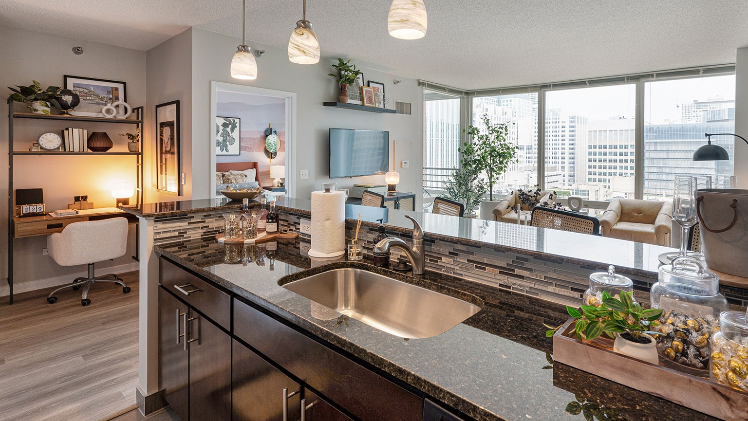 A view from the kitchen into an open-concept living area with a dedicated desk and shelving for a home office at The Streeter in Chicago