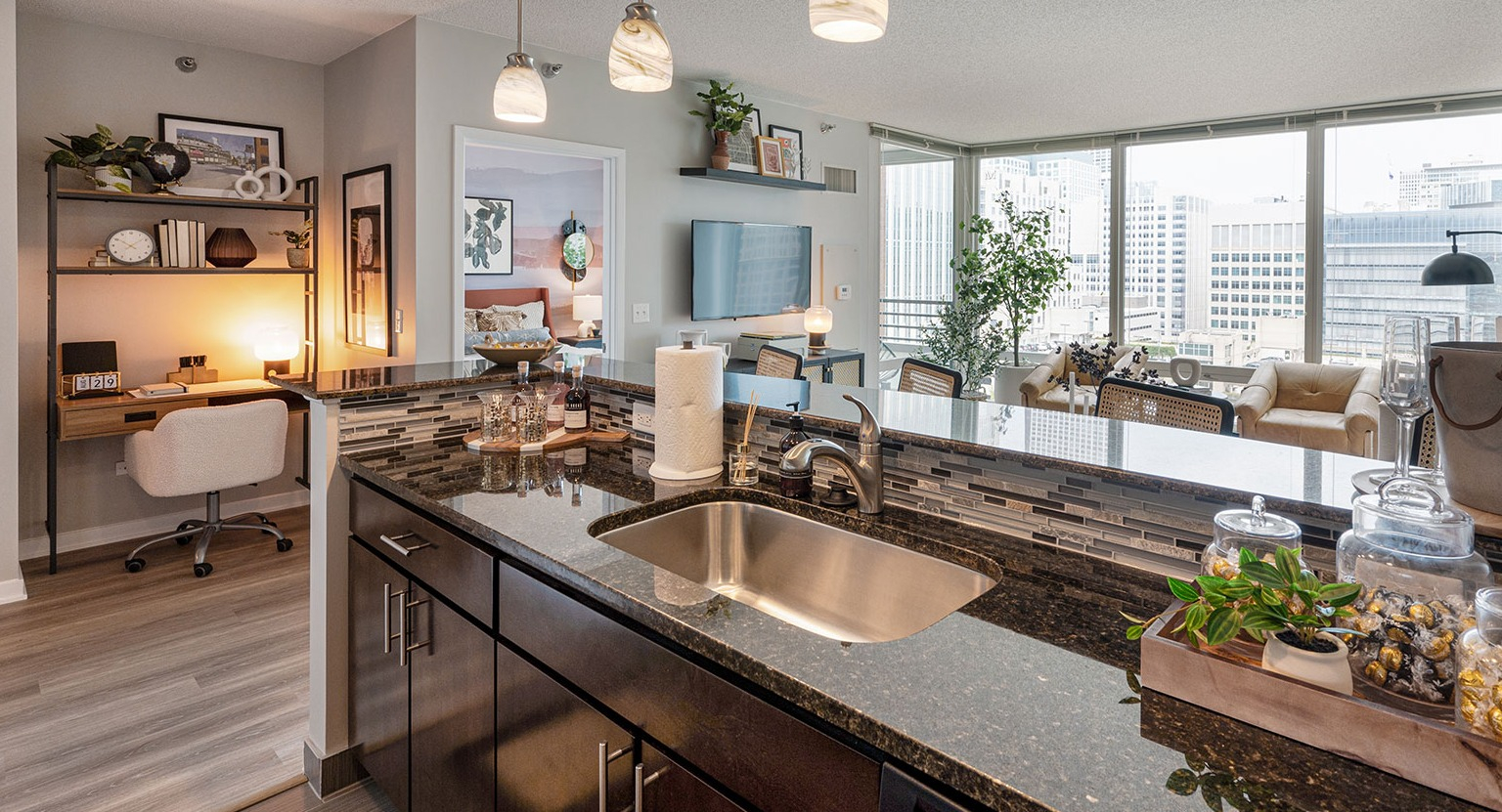 A view from the kitchen into an open-concept living area with a dedicated desk and shelving for a home office at The Streeter in Chicago