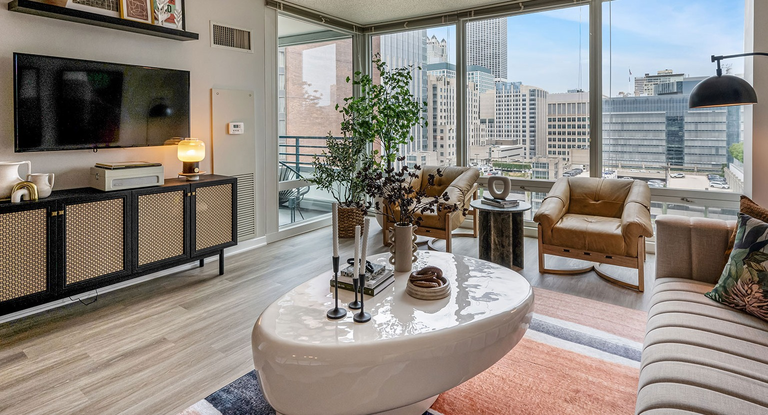 A stylish modern living room with comfortable seating, sleek furniture, and expansive city views from large windows at The Streeter in Chicago