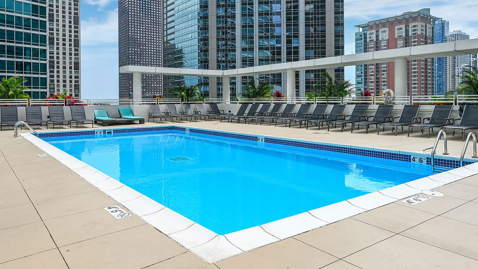 A vibrant outdoor swimming pool on a high-rise deck, surrounded by lounge chairs and tall city buildings at The Streeter in Chicago