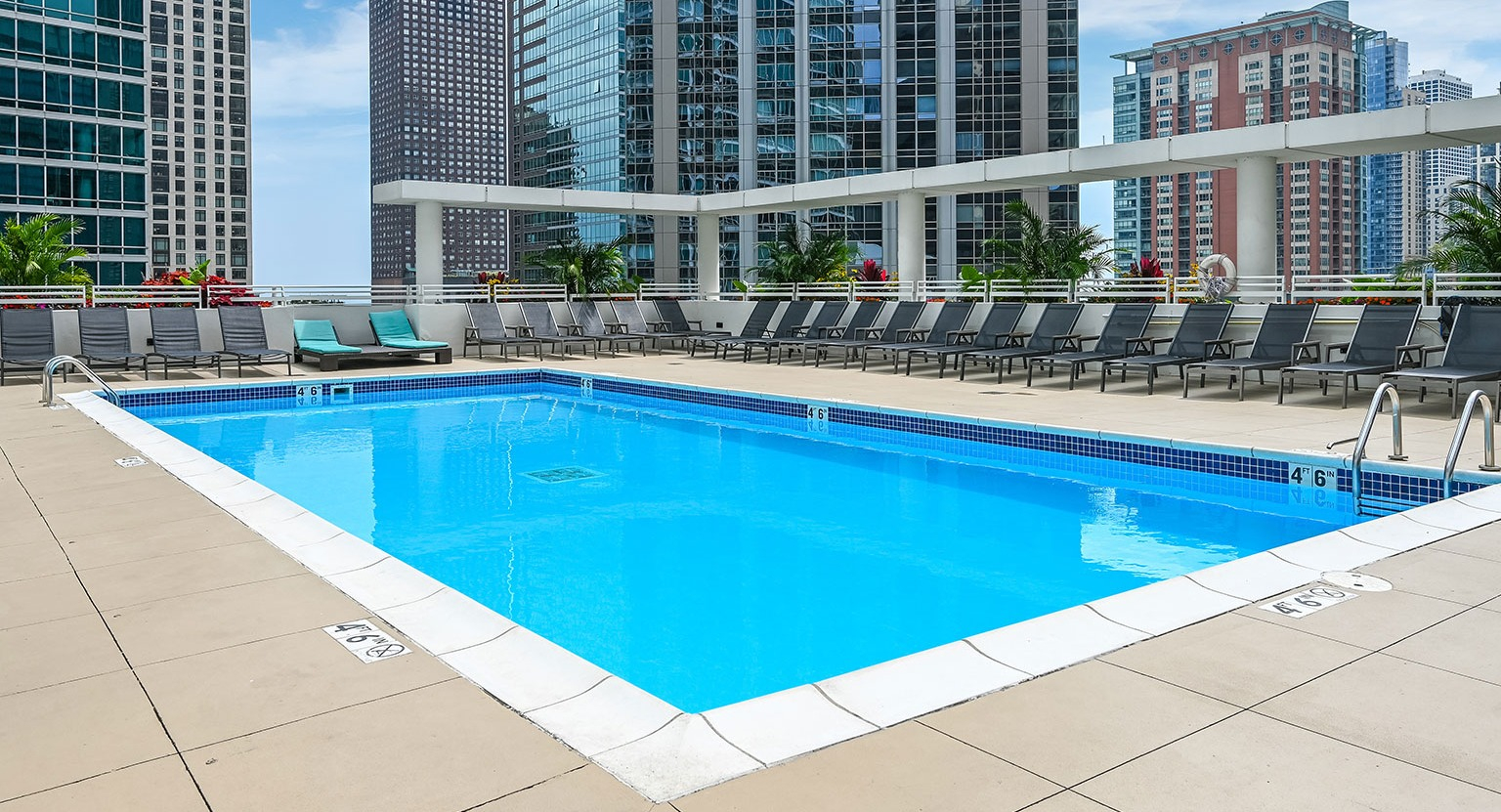 A vibrant outdoor swimming pool on a high-rise deck, surrounded by lounge chairs and tall city buildings at The Streeter in Chicago