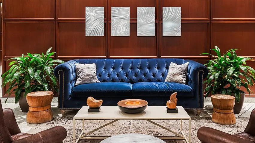A luxurious resident lounge featuring a vibrant blue velvet sofa, leather armchairs, and elegant wood paneling at The Streeter in Chicago