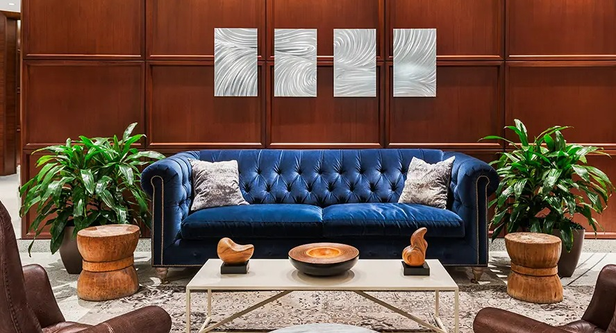 A luxurious resident lounge featuring a vibrant blue velvet sofa, leather armchairs, and elegant wood paneling at The Streeter in Chicago