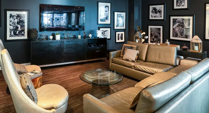 A cozy resident lounge doubling as a media room, featuring comfortable leather sofas and a large TV, adorned with classic photos at The Streeter in Chicago