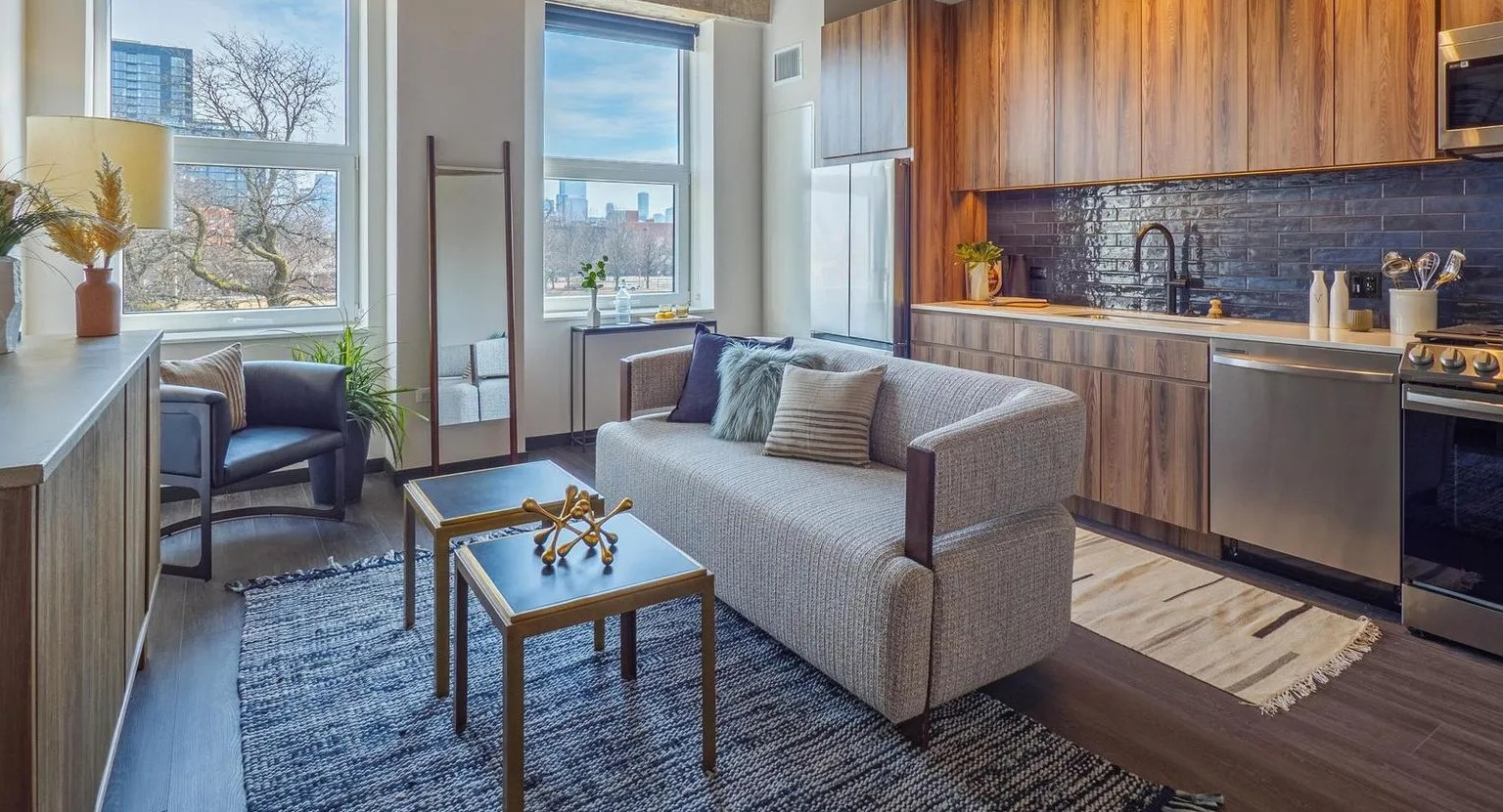 A stylish loft-style apartment featuring a modern kitchen with wood cabinets, a comfortable living area, and large windows at The Thompson at Fulton Market in Chicago
