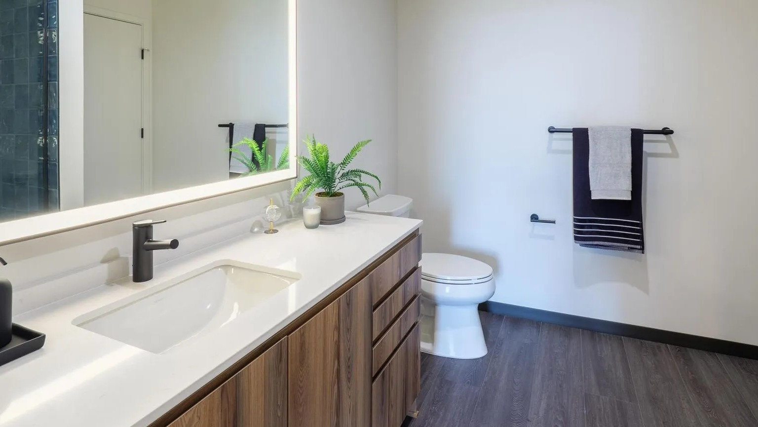 Contemporary bathroom with a wood vanity, white countertop, illuminated mirror, and a sleek walk-in shower at The Thompson at Fulton Market in Chicago