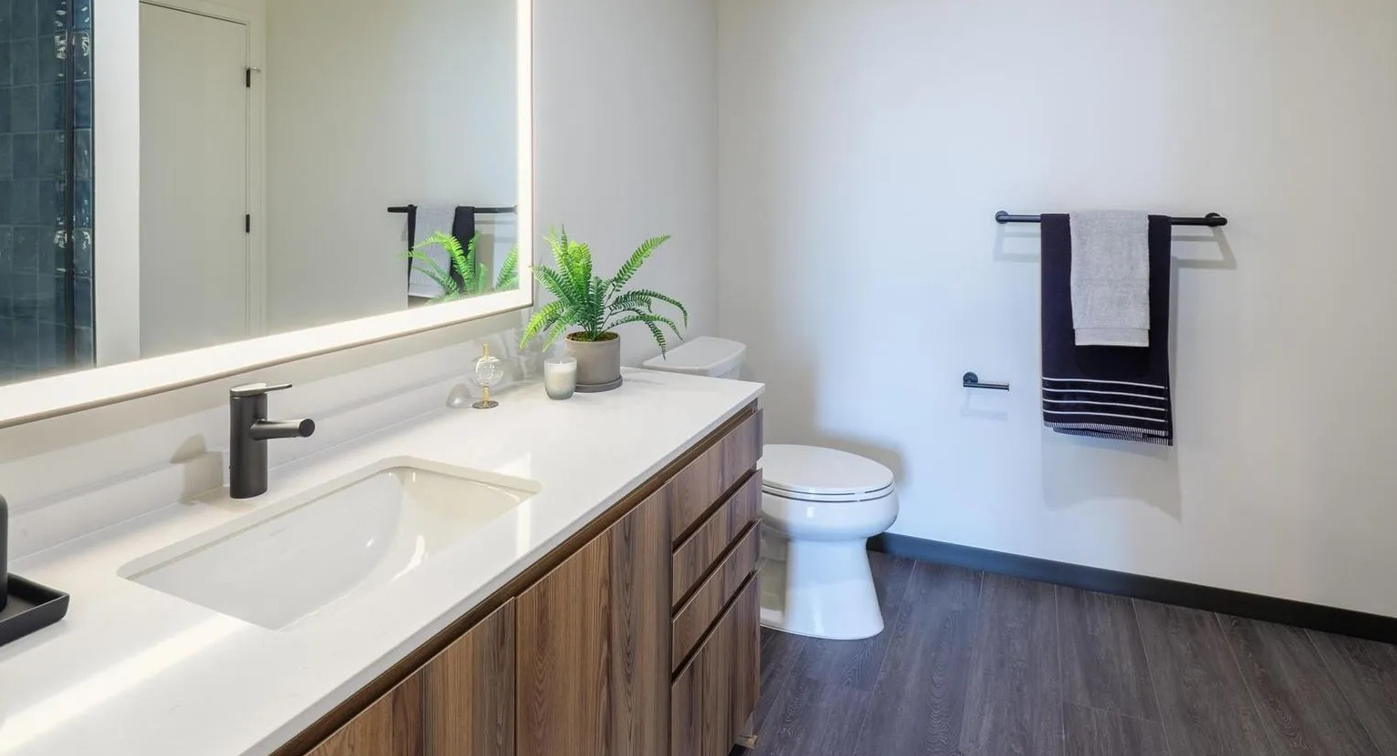 Contemporary bathroom with a wood vanity, white countertop, illuminated mirror, and a sleek walk-in shower at The Thompson at Fulton Market in Chicago