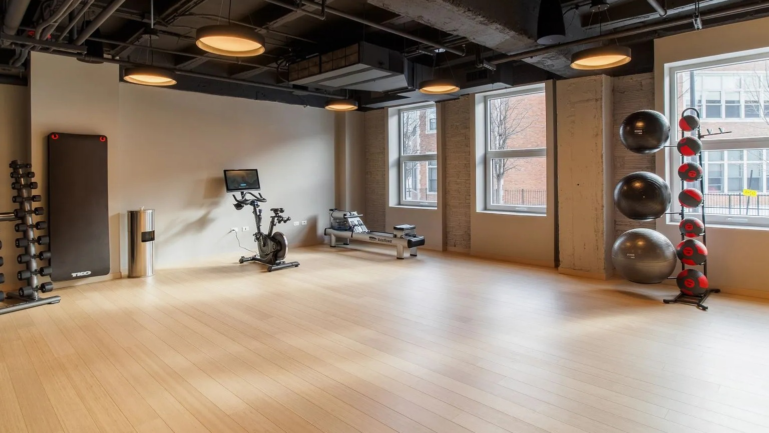 A bright and spacious fitness studio with hardwood floors, exercise bikes, and equipment for yoga or stretching at The Thompson at Fulton Market in Chicago