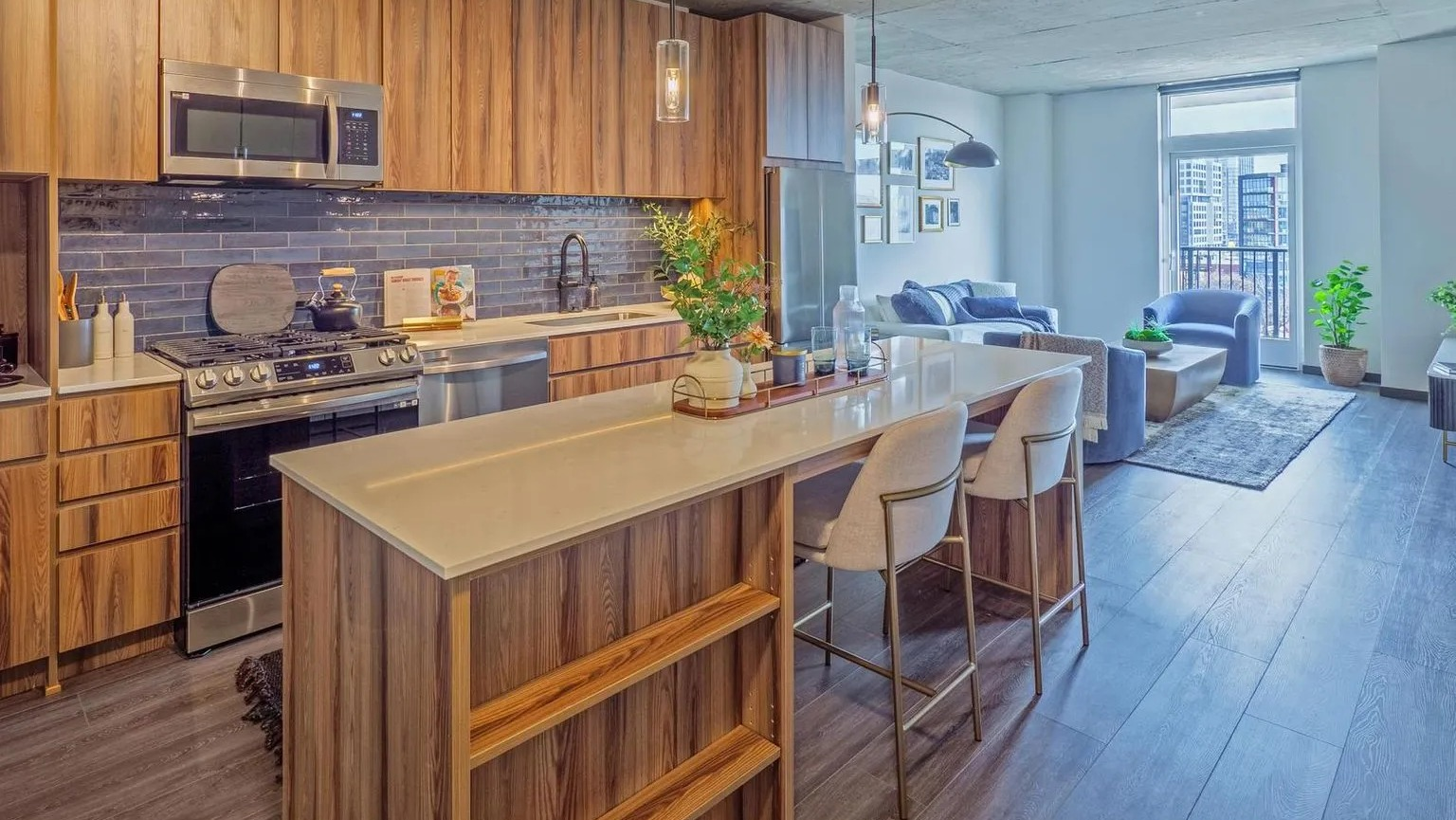A modern gourmet kitchen with rich wood cabinets, a large island with bar seating, and stainless steel appliances, open to a living area at The Thompson at Fulton Market in Chicago