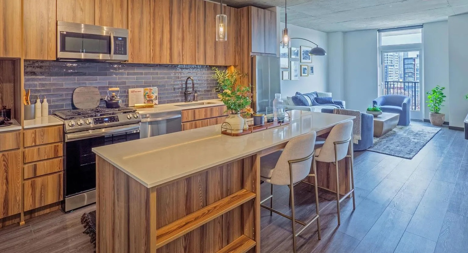 A modern gourmet kitchen with rich wood cabinets, a large island with bar seating, and stainless steel appliances, open to a living area at The Thompson at Fulton Market in Chicago