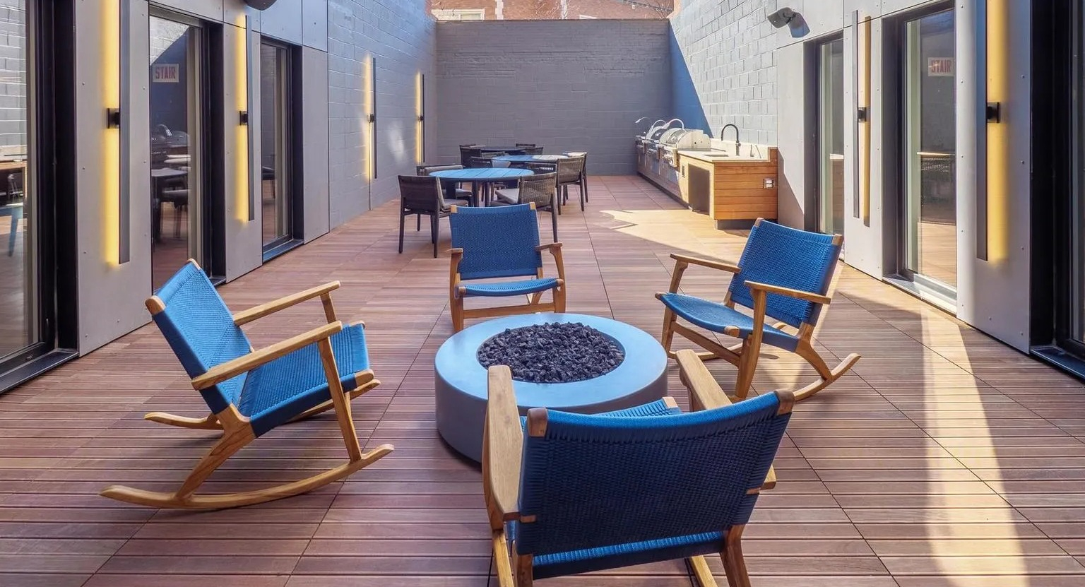 A chic outdoor patio featuring comfortable rocking chairs, a modern fire pit, and grilling stations, surrounded by brick buildings at The Thompson at Fulton Market in Chicago