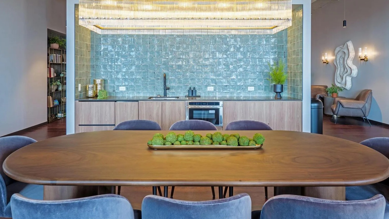 A luxurious resident lounge featuring a large dining table, a full kitchen area with teal tile, and comfortable seating at The Thompson at Fulton Market in Chicago