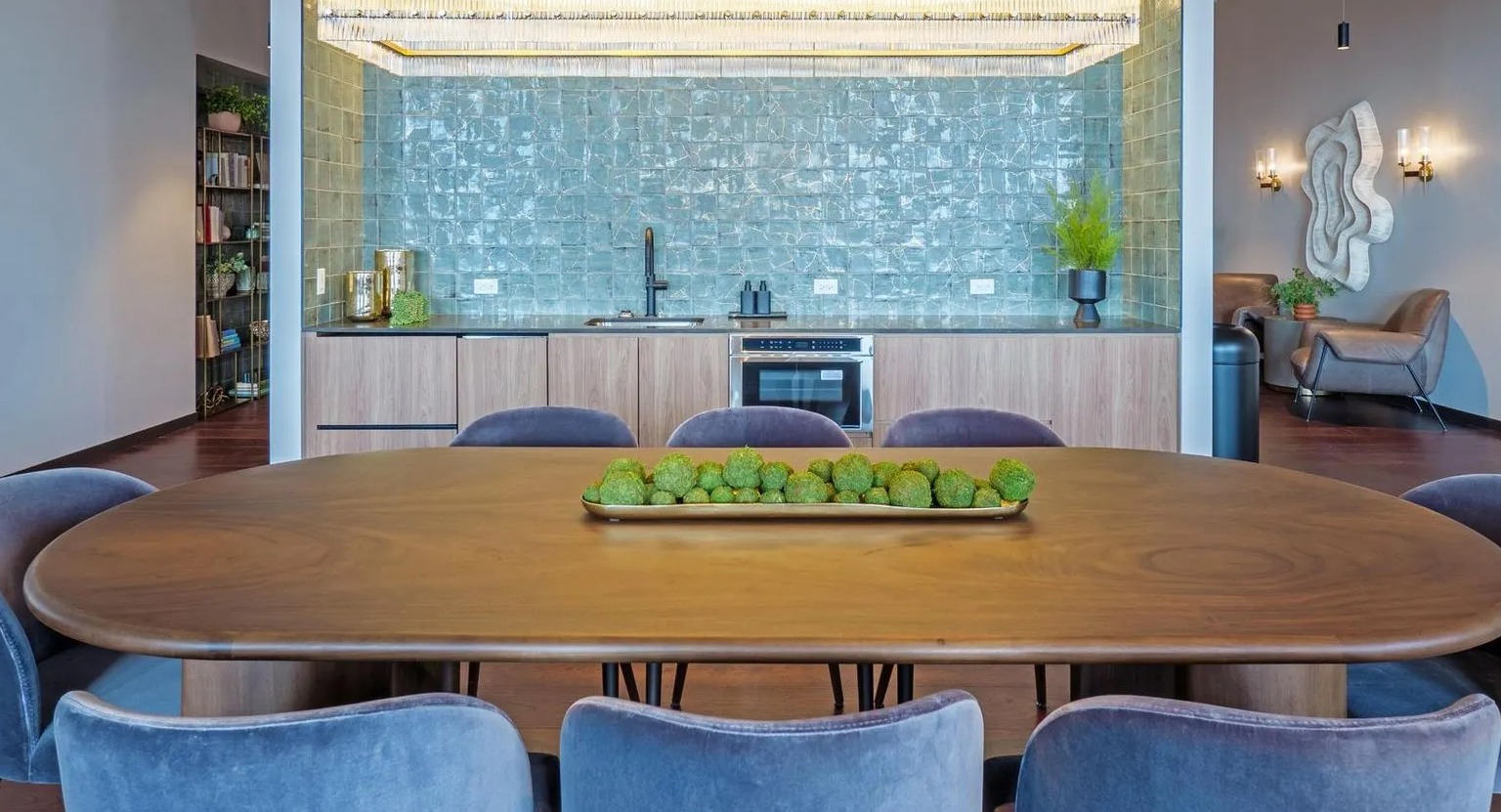 A luxurious resident lounge featuring a large dining table, a full kitchen area with teal tile, and comfortable seating at The Thompson at Fulton Market in Chicago