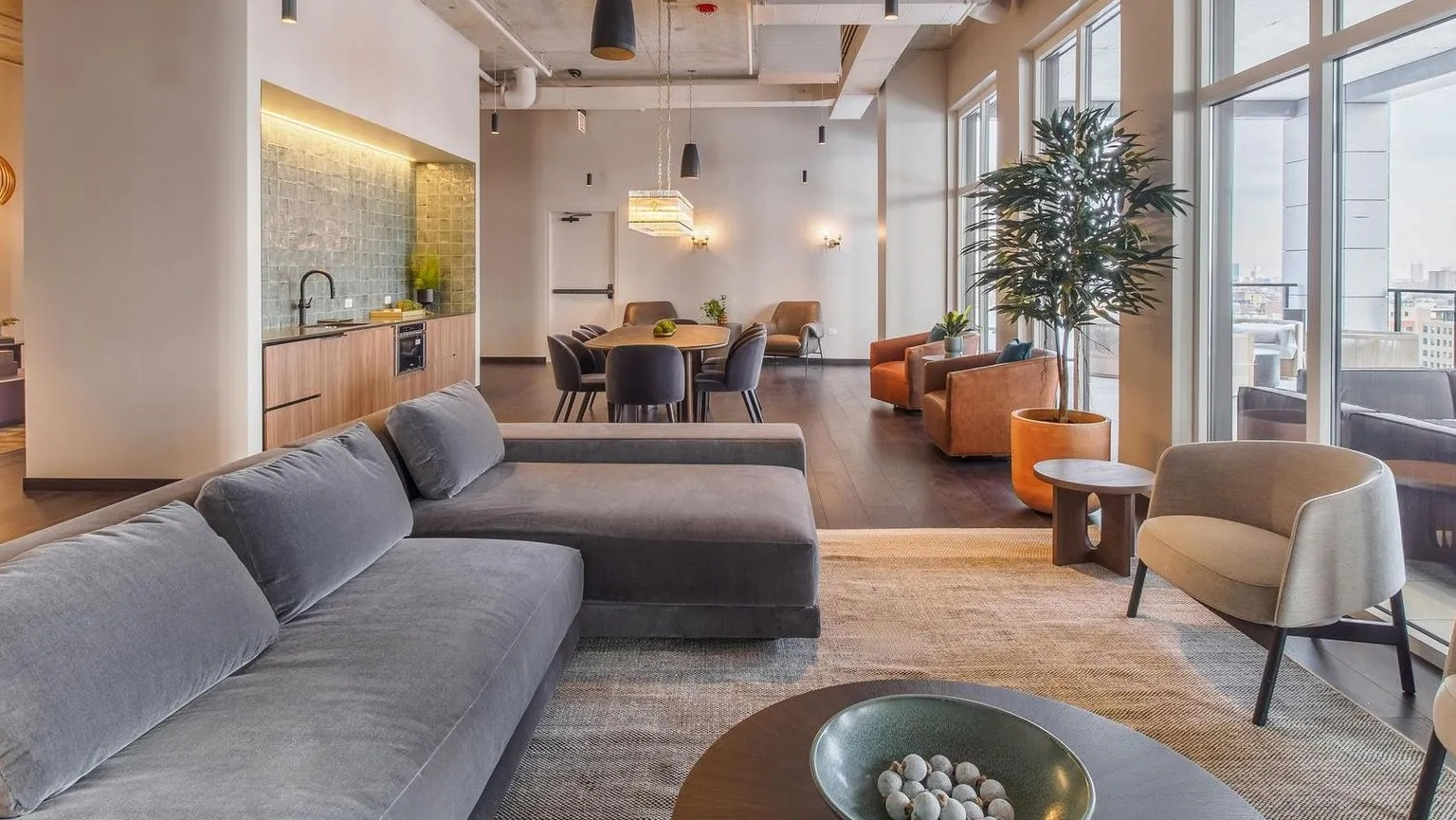A stylish resident lounge with comfortable seating, a dining area, and a modern kitchen space at The Thompson at Fulton Market in Chicago