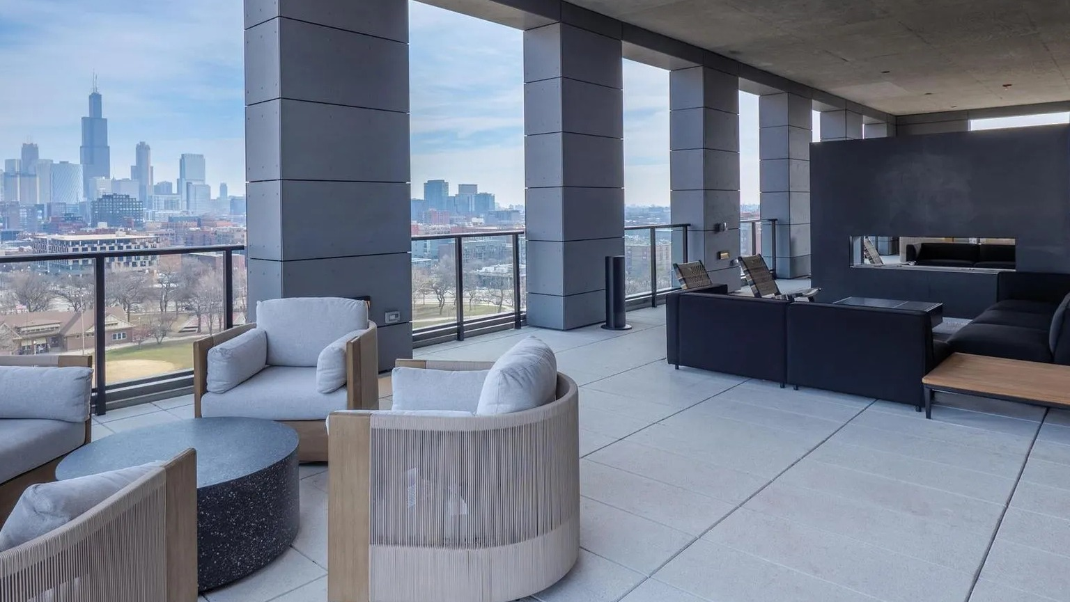 A modern rooftop lounge area with various seating arrangements, a fireplace, and panoramic views of the Chicago skyline at The Thompson at Fulton Market