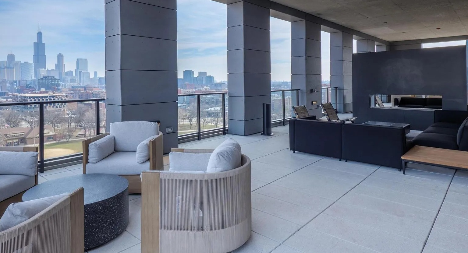 A modern rooftop lounge area with various seating arrangements, a fireplace, and panoramic views of the Chicago skyline at The Thompson at Fulton Market