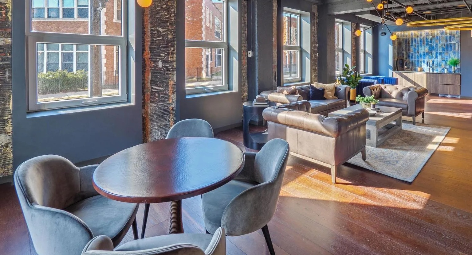 A trendy resident lounge and co-working space with a communal table, comfortable seating, and exposed brick walls at The Thompson at Fulton Market in Chicago