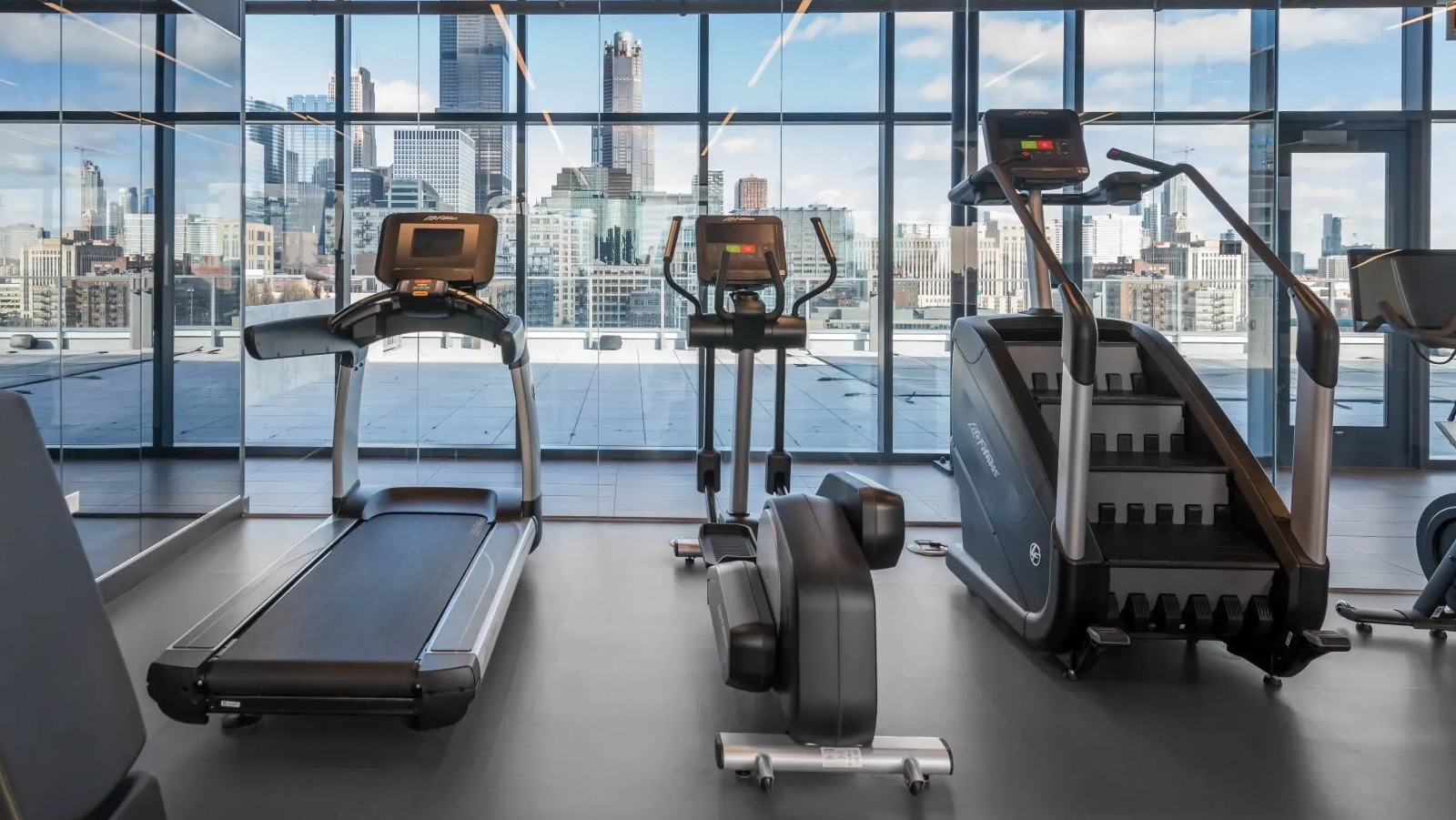 Modern fitness center with cardio machines, including treadmills and stair climbers, offering panoramic city views at The Van Buren in Chicago