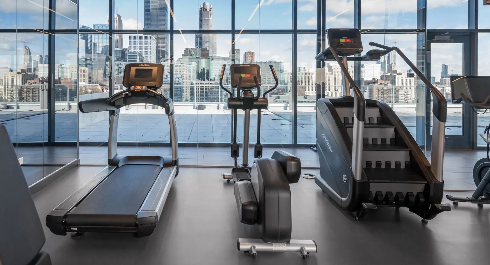 Modern fitness center with cardio machines, including treadmills and stair climbers, offering panoramic city views at The Van Buren in Chicago