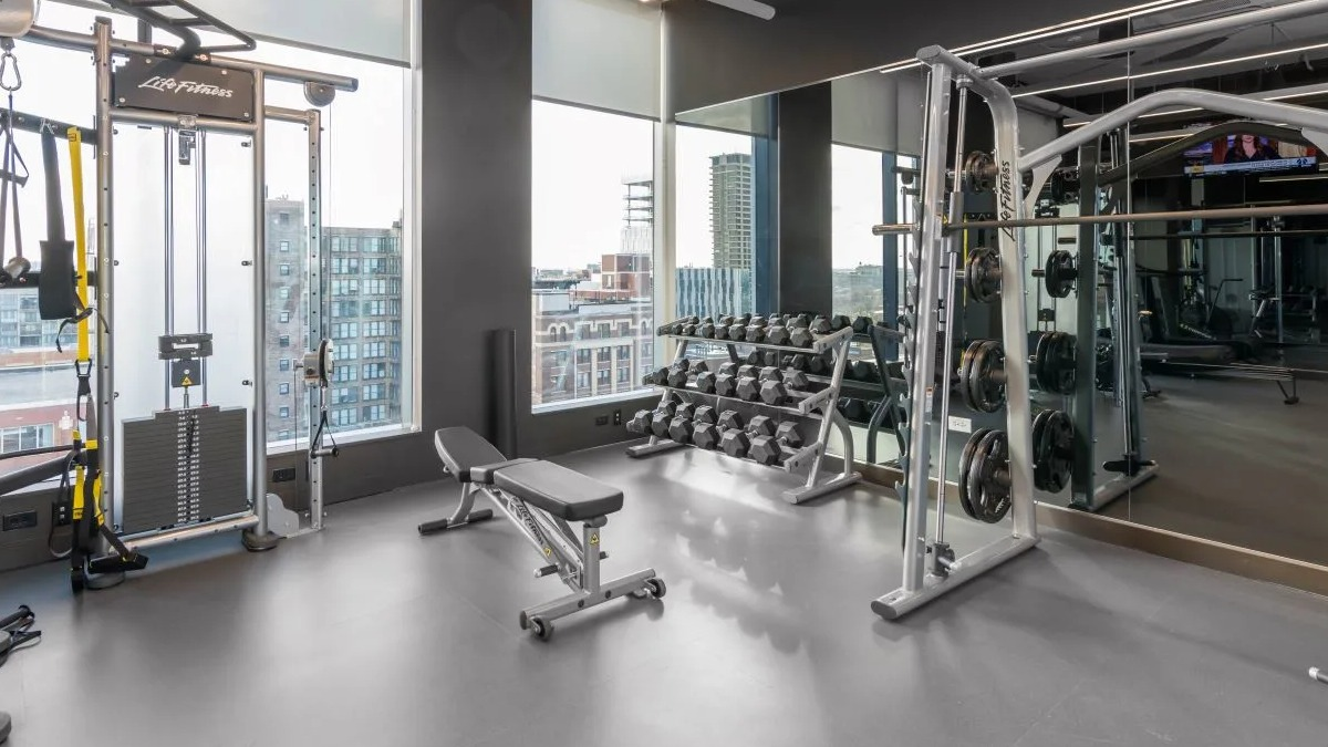 Well-equipped gym area featuring various weight training machines, free weights, and ample space for strength workouts at The Van Buren in Chicago