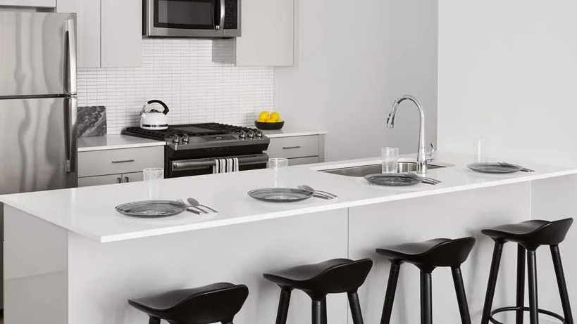 Bright kitchen with white cabinetry, stainless steel appliances, a large island with bar seating, and pendant lighting at The Van Buren in Chicago