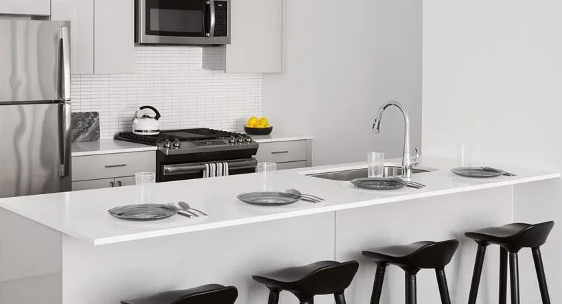 Bright kitchen with white cabinetry, stainless steel appliances, a large island with bar seating, and pendant lighting at The Van Buren in Chicago