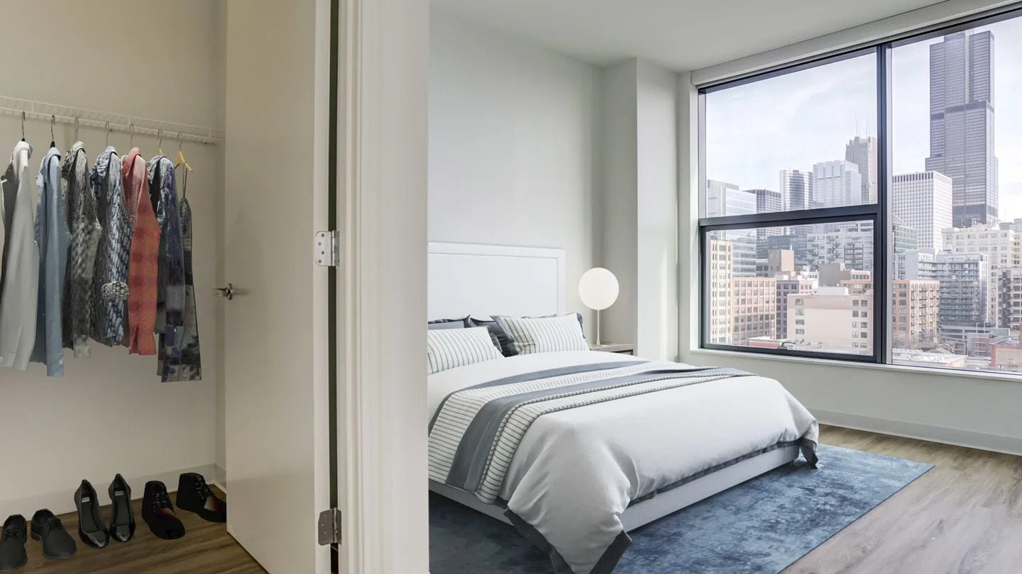 Spacious primary bedroom with a large window offering city views and an adjacent walk-in closet at The Van Buren apartments