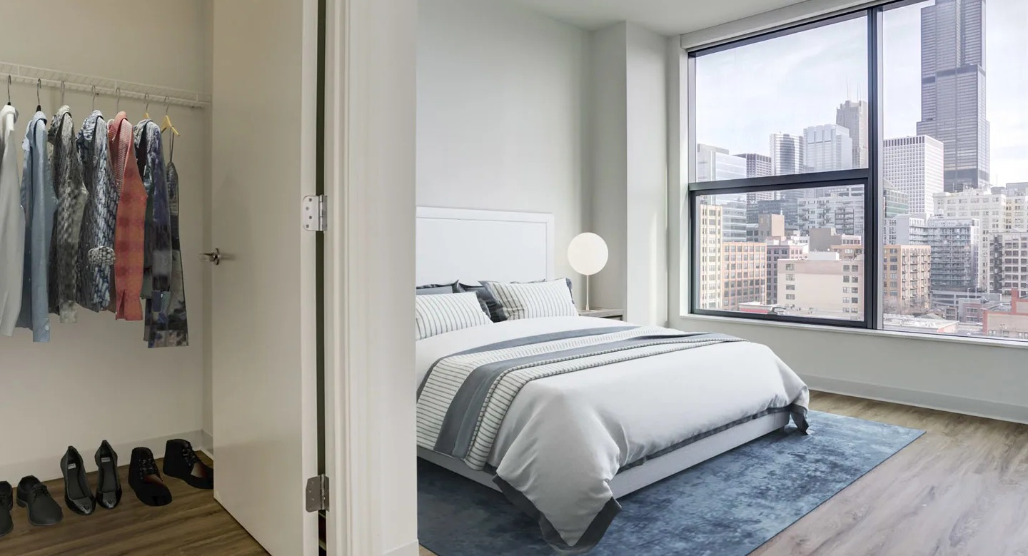 Spacious primary bedroom with a large window offering city views and an adjacent walk-in closet at The Van Buren apartments