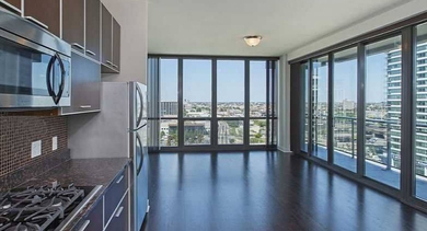 Chic kitchen with dark cabinetry, stainless steel appliances, and a spacious living area with a balcony view at Trio Apartments