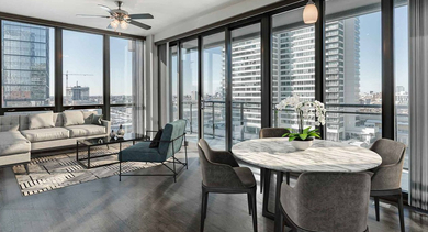 Spacious open-concept living and dining area with modern furniture and floor-to-ceiling windows showcasing high-rise city views at Trio Apartments in Chicago