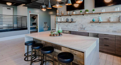 Modern resident lounge featuring a large island, bar seating, full kitchen amenities, and multiple screens for entertainment at Trio Apartments in Chicago