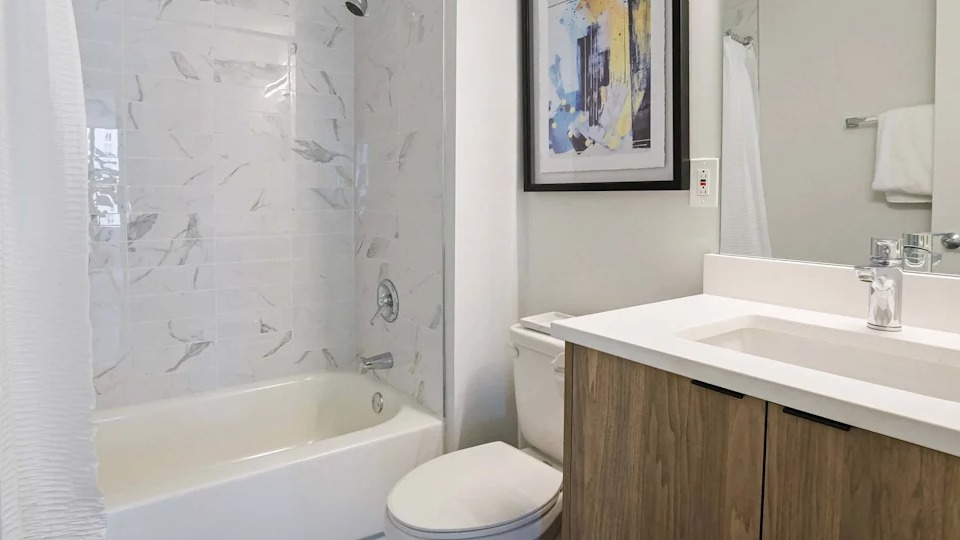 Clean and modern bathroom with a white vanity, spacious mirror, and a classic shower-over-tub design at Two East Oak in Chicago