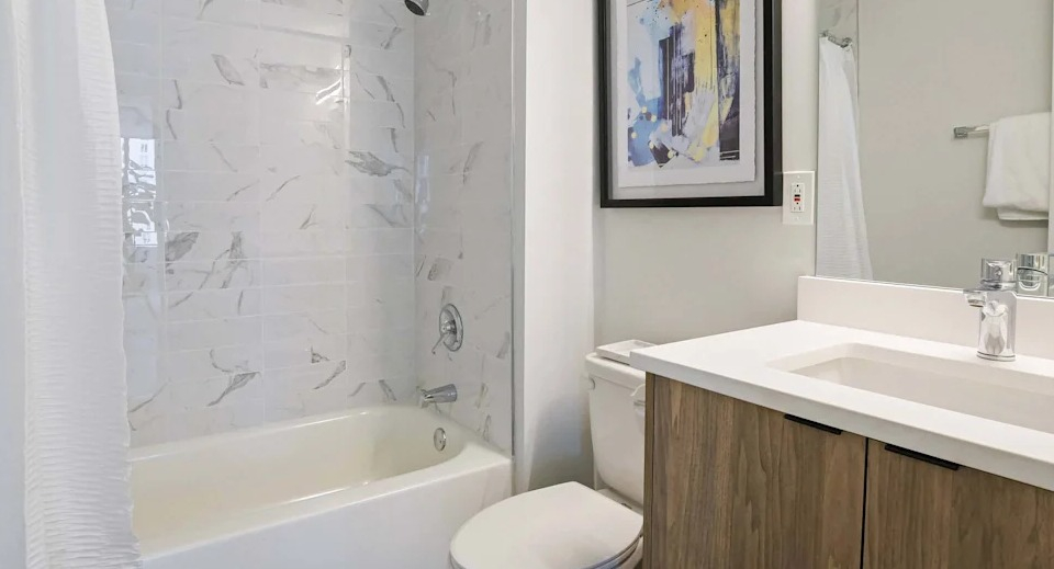 Clean and modern bathroom with a white vanity, spacious mirror, and a classic shower-over-tub design at Two East Oak in Chicago