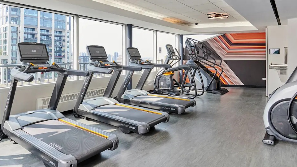 Modern fitness center equipped with multiple treadmills and cardio machines, offering city views through large windows at Two East Oak in Chicago